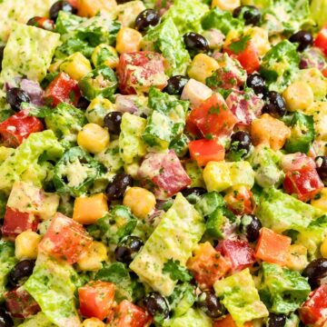 Southwest chopped salad in a white bowl with romaine, black beans, corn, tomatoes, bell peppers, jalapeƱos, red onion, cilantro, and creamy salsa ranch dressing, served with baked tortilla chips on the side.