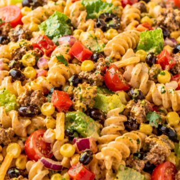 Southwest taco pasta salad with rotini, seasoned ground beef, corn, black beans, cherry tomatoes, romaine, red onion, cheddar, cilantro, and creamy taco dressing in a white bowl.