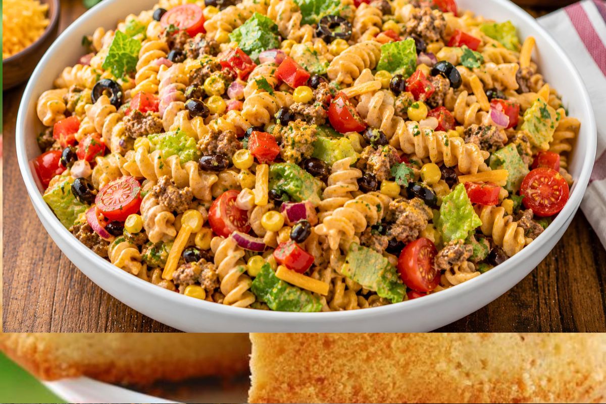 Southwest taco pasta salad in a white bowl with rotini, seasoned ground beef, corn, black beans, cherry tomatoes, romaine, red onion, cheddar cheese, cilantro, and creamy taco dressing on a wooden table.