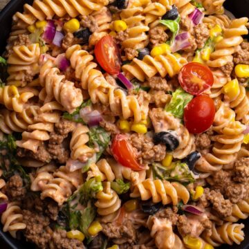 Close-up of taco pasta salad with ground beef, rotini, corn, tomatoes, black olives, red onion, lettuce, and creamy Southwest dressing.