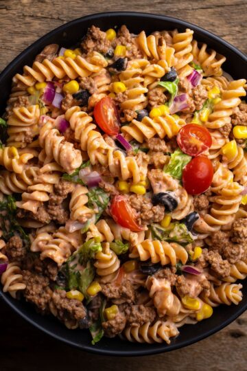 Close-up of taco pasta salad with ground beef, rotini, corn, tomatoes, black olives, red onion, lettuce, and creamy Southwest dressing.