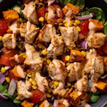 Close-up of a chicken taco sweet potato protein bowl with black beans, corn, tomatoes, red onion, roasted sweet potatoes, and creamy dressing.