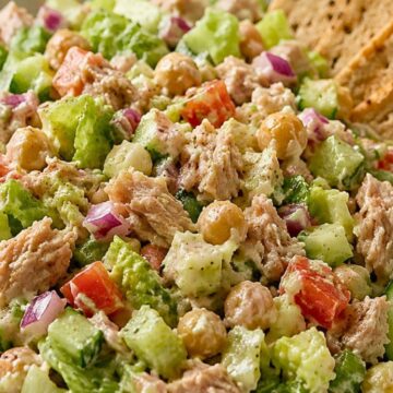 Tuna chopped salad with chickpeas, romaine lettuce, cucumber, red onion, tomato, and creamy dressing in a white bowl, served with crisp crackers on the side.
