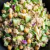 Tuna chopped salad with chickpeas, cucumbers, romaine lettuce, red onion, fresh dill, and creamy dressing in a black bowl.