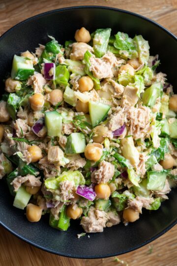 Tuna chopped salad with chickpeas, cucumbers, romaine lettuce, red onion, fresh dill, and creamy dressing in a black bowl.