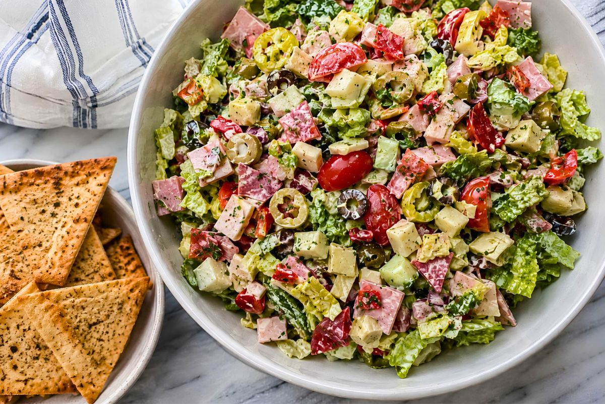 Antipasto grinder chopped salad with romaine, ham, salami, provolone, tomatoes, cucumbers, artichokes, roasted red peppers, banana peppers, and olives in creamy dressing, served with seasoned garlic pita chips.
