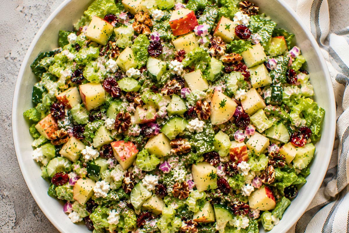Overhead view of apple pecan salad with chopped romaine, red apples, cucumber, celery, dried cranberries, feta cheese, red onion, and toasted pecans tossed in creamy apple cider dressing.