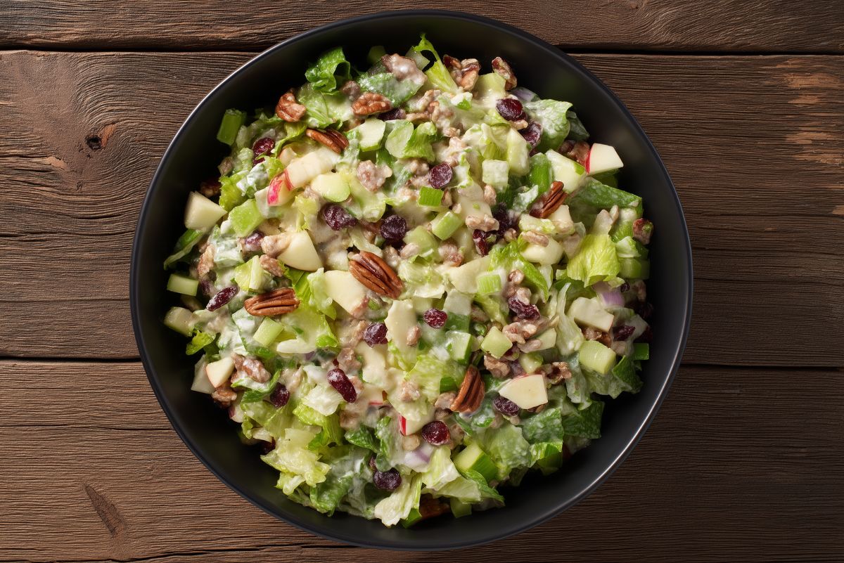Apple pecan salad with chopped lettuce, diced apples, pecans, dried cranberries, celery, and creamy cider dressing in a black bowl.