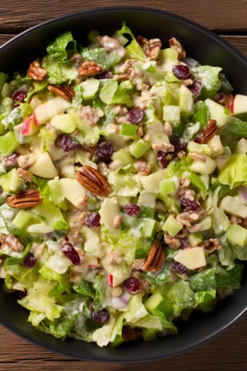 Close-up of apple pecan salad with crisp lettuce, apples, pecans, dried cranberries, celery, and creamy cider dressing.