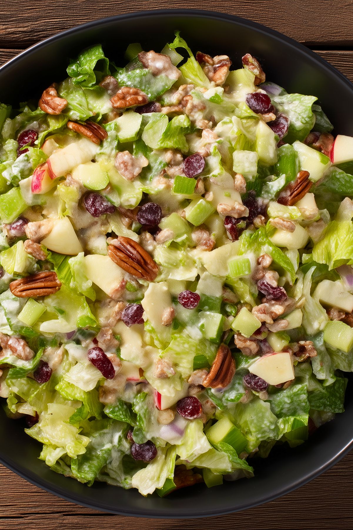 Close-up of apple pecan salad with crisp lettuce, apples, pecans, dried cranberries, celery, and creamy cider dressing.