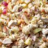 Close-up of creamy chicken bacon apple pasta salad with rotini, chicken, red apples, celery, red onion, cranberries, and crisp bacon in a black bowl.
