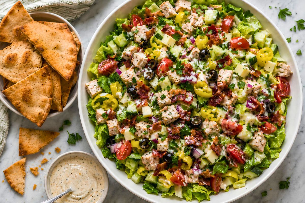 Chicken bacon grinder chopped salad with romaine, chicken breast, turkey bacon, provolone, cucumbers, tomatoes, banana peppers, black olives, red onion, and creamy dressing, served with large homemade garlic pita chips and extra dressing.
