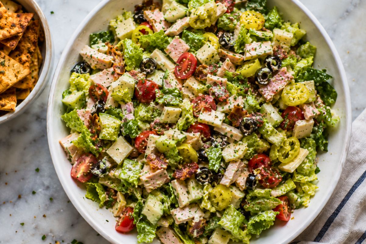 Club grinder chopped salad with romaine, turkey, ham, provolone, cherry tomatoes, cucumbers, black olives, banana peppers, bacon, herbs, and creamy dressing, served with garlic pita chips.