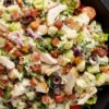 Close-up of club grinder chopped salad with turkey, bacon, lettuce, tomatoes, cucumbers, black olives, red onion, cheese, and creamy dressing in a black bowl.