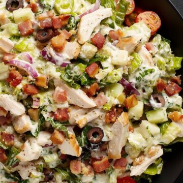 Close-up of club grinder chopped salad with turkey, bacon, lettuce, tomatoes, cucumbers, black olives, red onion, cheese, and creamy dressing in a black bowl.