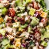 Close-up of cranberry turkey club chopped salad with chopped romaine, turkey breast, crispy bacon, cheddar cheese, cucumbers, cherry tomatoes, red onion, dried cranberries, and creamy dressing.