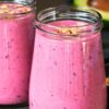 Creamy berry avocado smoothie in glass jars with a pink fruit blend, topped with oats or granola, with blueberries, a striped straw, and sliced avocado in the background.