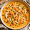 Creamy chicken and butternut squash soup with shredded chicken, squash cubes, carrots, celery, parsley, and black pepper in a rustic bowl, served with crusty bread.