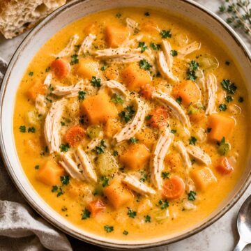 Creamy chicken and butternut squash soup with shredded chicken, squash cubes, carrots, celery, parsley, and black pepper in a rustic bowl, served with crusty bread.