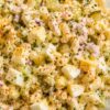 Close-up of creamy deviled egg pasta salad with elbow macaroni, chopped hard-boiled eggs, celery, dill pickles, red onion, fresh herbs, and paprika in a glass bowl.
