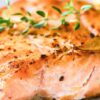 Grilled lemon garlic herb salmon fillet with a golden seared top, sliced garlic, black pepper, and fresh thyme garnish on a white plate.