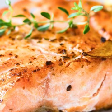 Grilled lemon garlic herb salmon fillet with a golden seared top, sliced garlic, black pepper, and fresh thyme garnish on a white plate.
