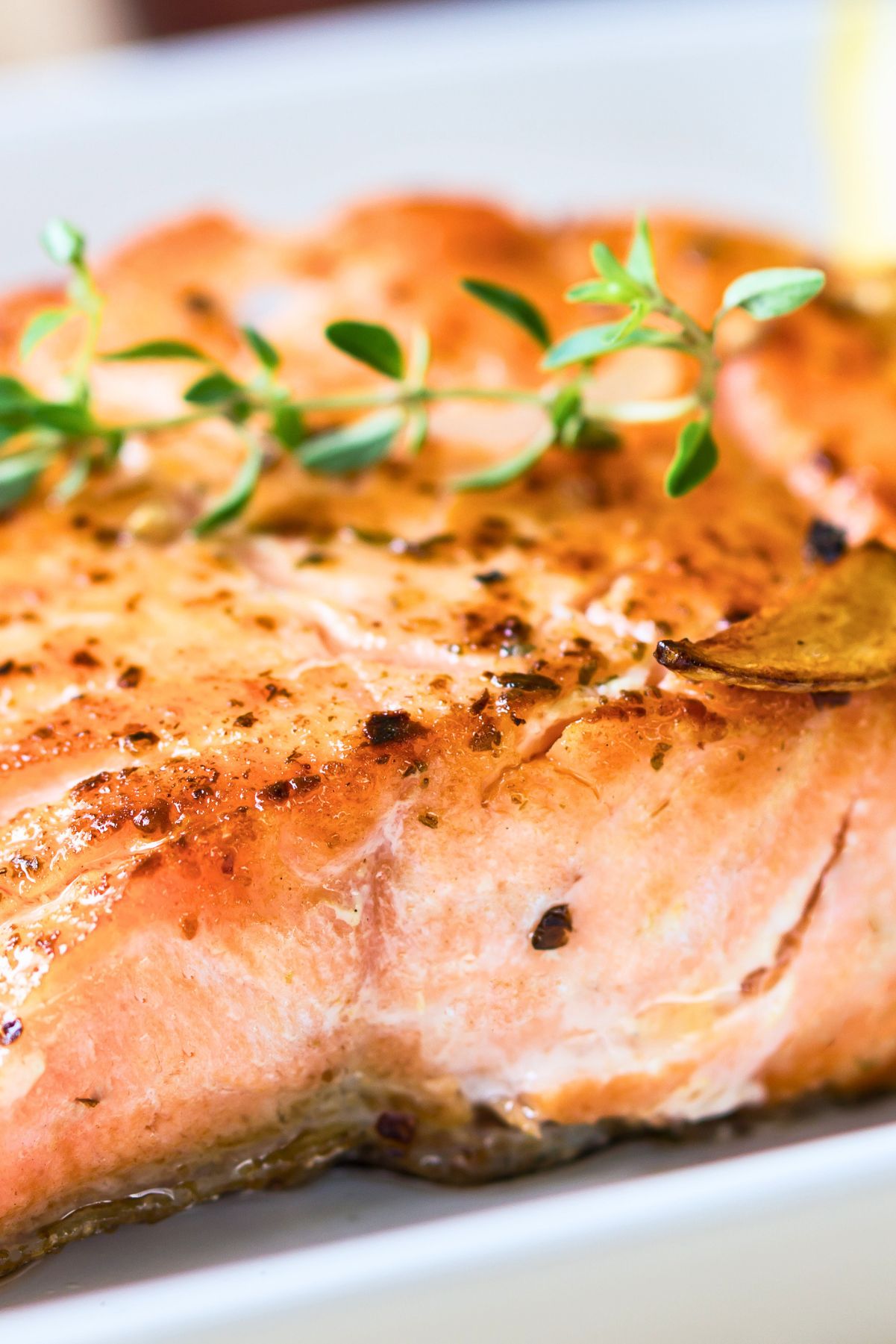 Grilled lemon garlic herb salmon fillet with a golden seared top, sliced garlic, black pepper, and fresh thyme garnish on a white plate.