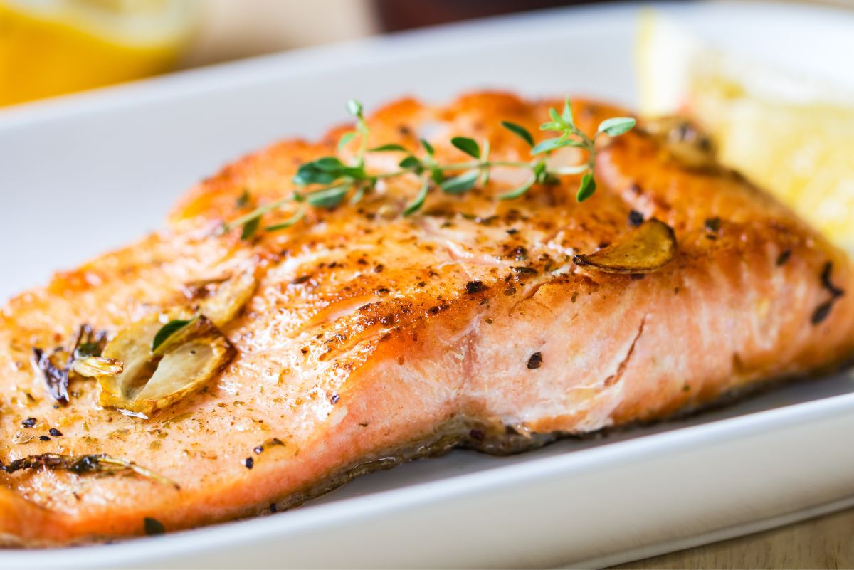 Grilled lemon garlic herb salmon fillet with a golden seared crust, sliced garlic, black pepper, fresh thyme garnish, and lemon wedges on a white plate.