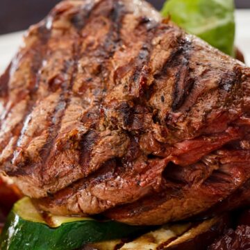 Grilled sirloin steak with dark grill marks served over sliced zucchini and eggplant, with roasted red pepper and chunky balsamic tomato-onion jam on a white plate.