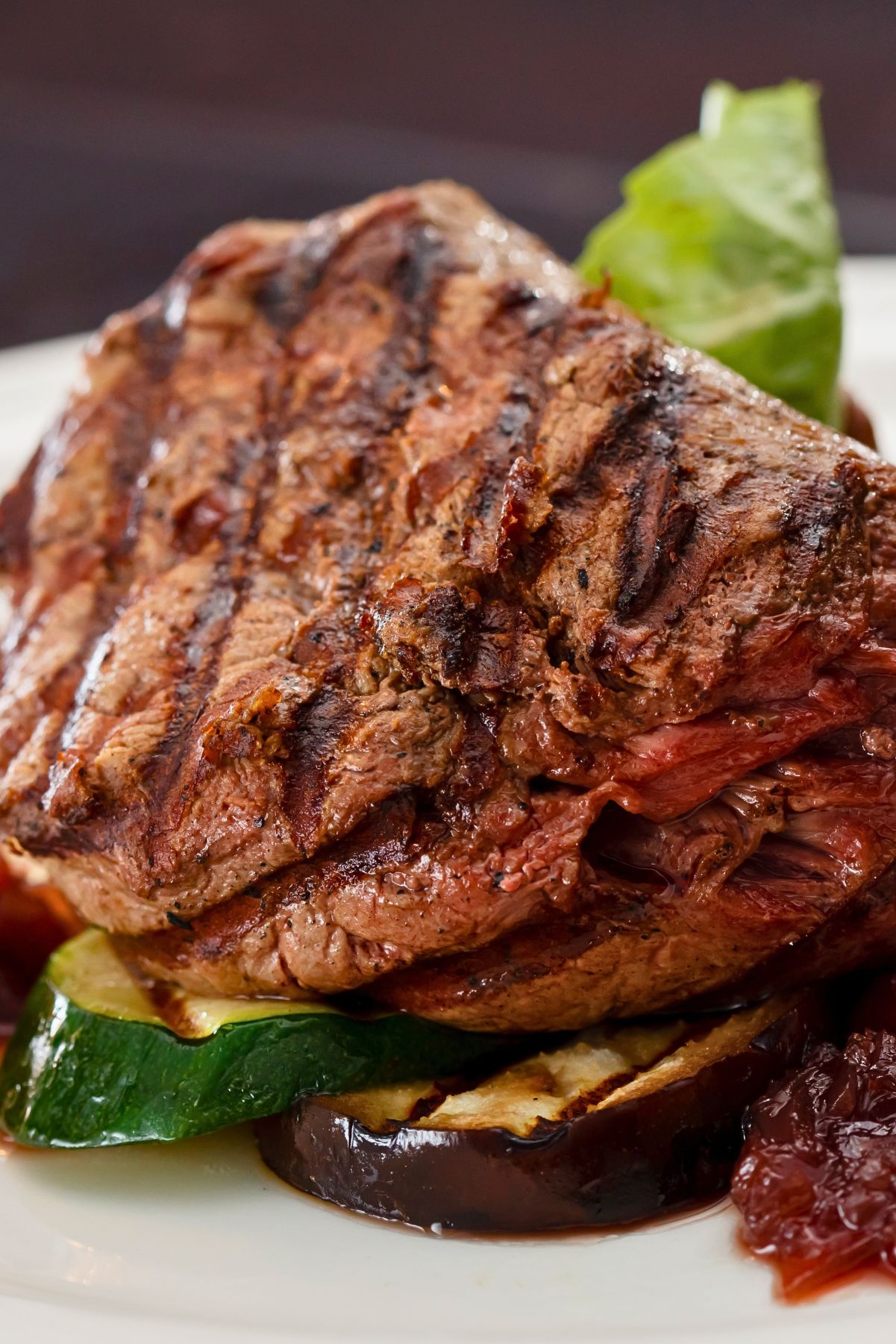 Grilled sirloin steak with dark grill marks served over sliced zucchini and eggplant, with roasted red pepper and chunky balsamic tomato-onion jam on a white plate.
