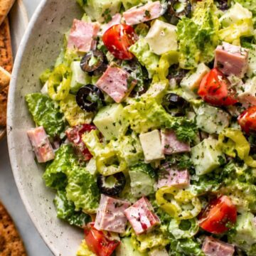 Creamy ham and provolone grinder chopped salad with romaine lettuce, cucumber, cherry tomatoes, banana peppers, black olives, herbs, and garlic pita chips served on the side.