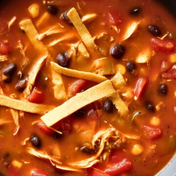 Hearty chicken tortilla soup with shredded chicken, black beans, corn, tomatoes, and crispy tortilla strips in a black bowl.
