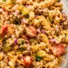 High protein cheeseburger pasta salad with rotini, seasoned ground beef, cheddar cheese, cherry tomatoes, dill pickles, red onion, parsley, and creamy cheeseburger dressing in a glass serving bowl.