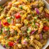 Close-up of high protein cheeseburger pasta salad with rotini, ground beef, shredded cheddar, tomatoes, red onion, pickles, and creamy dressing.