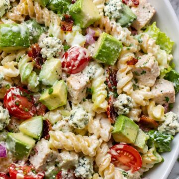 High protein Chicken Cobb pasta salad with rotini, grilled chicken, turkey bacon, avocado, cherry tomatoes, cucumber, romaine, hard-boiled eggs, blue cheese crumbles, red onion, and creamy dressing.