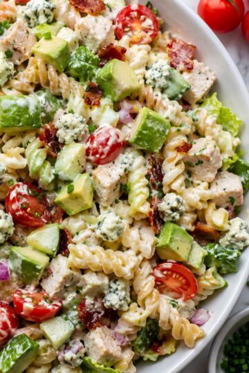 High protein Chicken Cobb pasta salad with rotini, grilled chicken, turkey bacon, avocado, cherry tomatoes, cucumber, romaine, hard-boiled eggs, blue cheese crumbles, red onion, and creamy dressing.