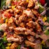 Close-up of a high protein chicken taco salad bowl with seasoned chicken, lettuce, black beans, corn, tomatoes, red onion, and creamy taco dressing.
