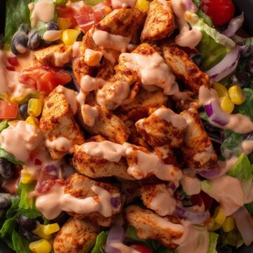 Close-up of a high protein chicken taco salad bowl with seasoned chicken, lettuce, black beans, corn, tomatoes, red onion, and creamy taco dressing.