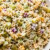 Creamy dill pickle rotini pasta salad with chopped pickles, cucumber, cheddar cheese, red onion, and fresh dill in a white serving bowl.
