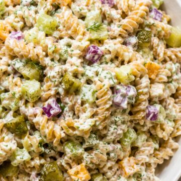 Creamy dill pickle rotini pasta salad with chopped pickles, cucumber, cheddar cheese, red onion, and fresh dill in a white serving bowl.