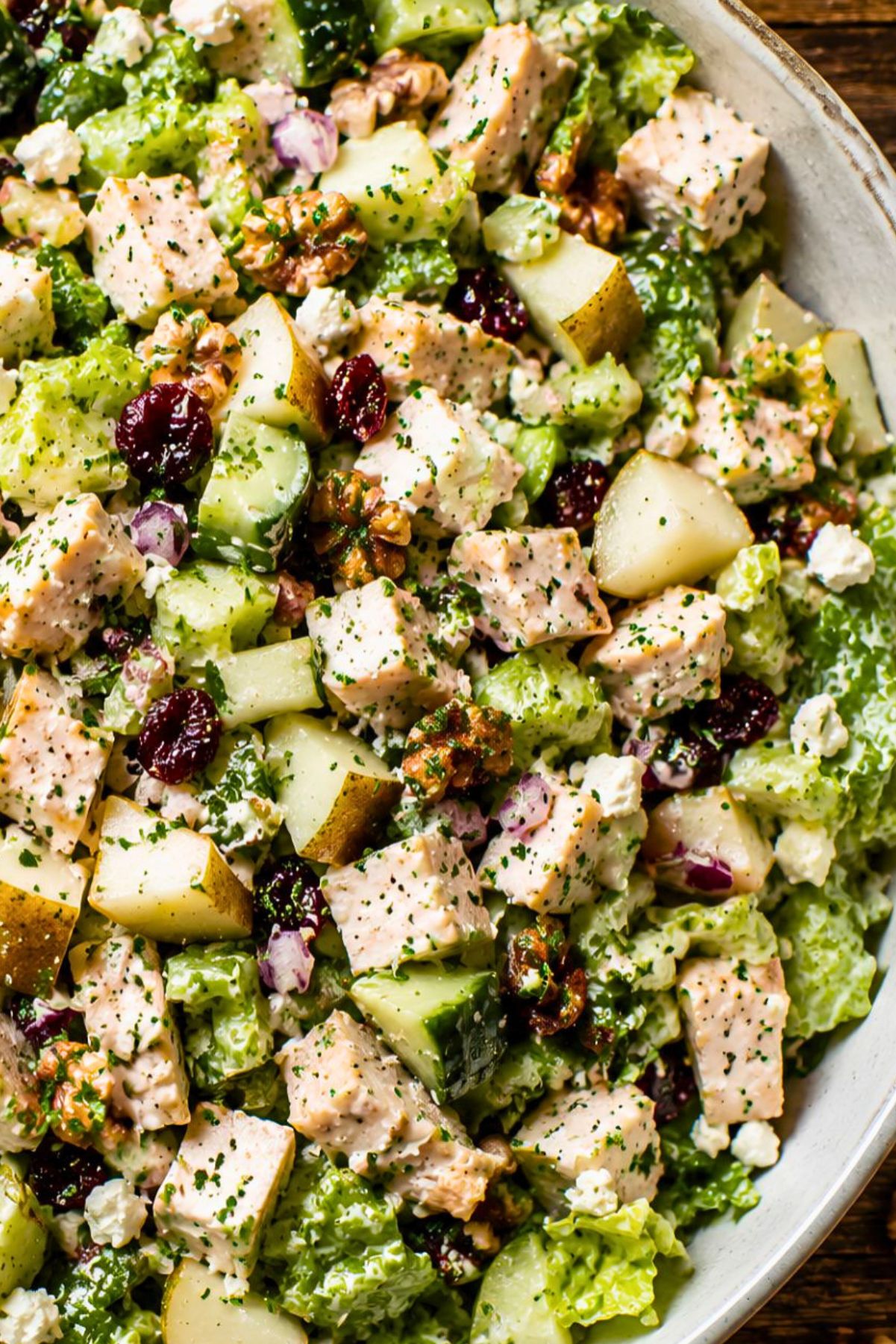 Close-up of pear walnut chicken chopped salad with romaine lettuce, cucumber, celery, diced pear, dried cranberries, red onion, feta cheese, walnuts, and chicken tossed in creamy balsamic Dijon dressing.