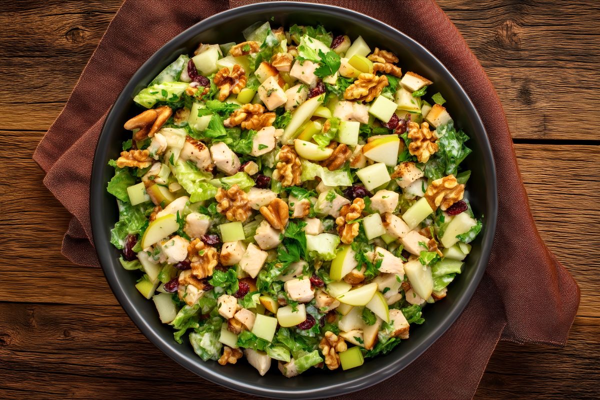 Pear walnut chicken chopped salad with diced chicken, fresh pears, walnuts, dried cranberries, chopped lettuce, and creamy dressing in a black bowl.