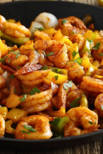Close-up of Cajun shrimp and pepper skillet with seasoned shrimp, yellow and green bell peppers, onions, and fresh herbs.