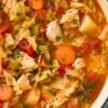 Close-up of rustic chicken cabbage and tomato soup with tender chicken, chopped cabbage, carrots, celery, potatoes, diced tomatoes, parsley, and a bay leaf in a rich tomato broth.
