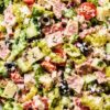 Spicy Italian Grinder Chopped Salad with chopped romaine, deli meats, provolone cheese, cherry tomatoes, cucumbers, banana peppers, black olives, red onion, herbs, and creamy grinder dressing in a large bowl.