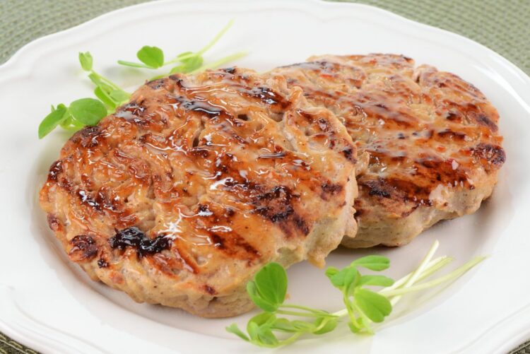 Two grilled sweet chili glazed turkey patties with browned edges and glossy sauce, served on a white plate with fresh green sprouts.