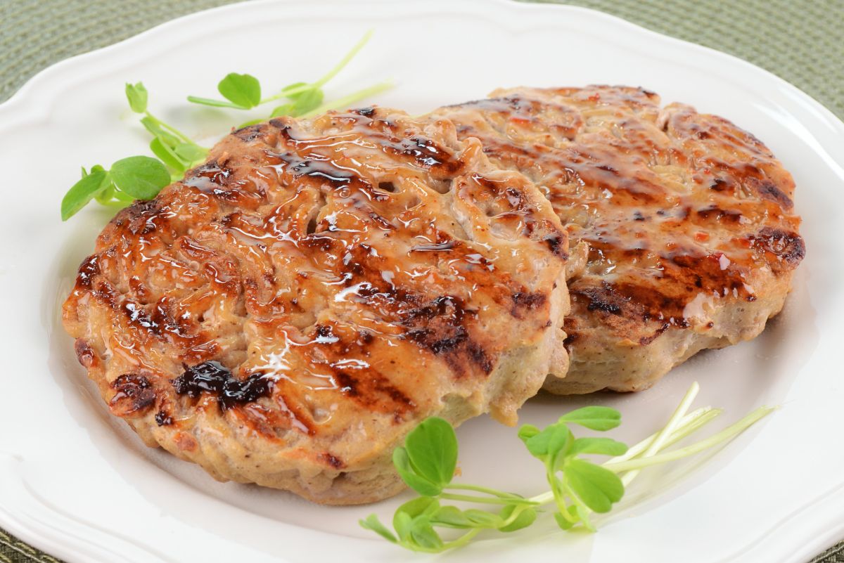 Two grilled sweet chili glazed turkey patties with browned edges and glossy sauce, served on a white plate with fresh green sprouts.