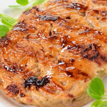 Close-up of sweet chili glazed turkey patties with browned grill marks and glossy sauce, served on a white plate with fresh green garnish.