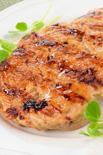 Close-up of sweet chili glazed turkey patties with browned grill marks and glossy sauce, served on a white plate with fresh green garnish.