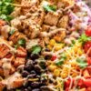 Tex-Mex chicken sweet potato bowl with grilled chicken, roasted sweet potatoes, black beans, corn, tomatoes, red onion, shredded cheese, romaine, cilantro, and creamy sauce.